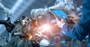 Robotic welding arm joining a steel frame, with a technician reviewing a tablet in the foreground